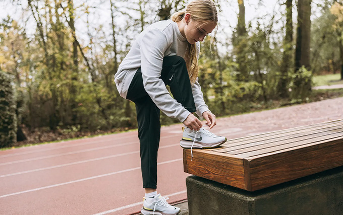 Femme debout qui fait ses lacets sur un banc